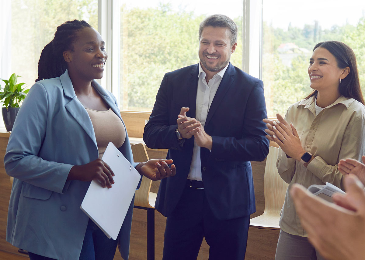 Three people in business attire standing, talking, and laughing together.