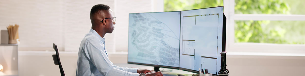 a man sits in front of a computer reviewing neighborhood plans and building blueprints on large computer monitors