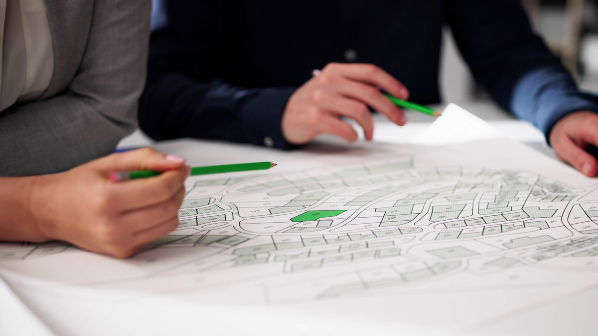 image of plans laid out on a table with two poeple's hands resting on the plans while reviewing them