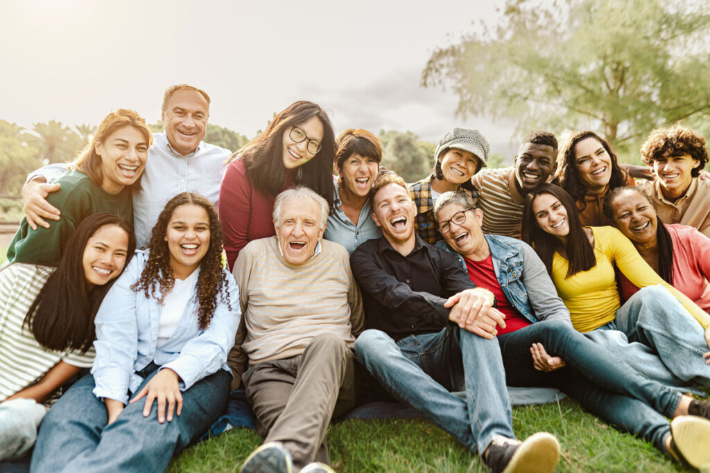 Large group of people sitting on the grass together, smiling.