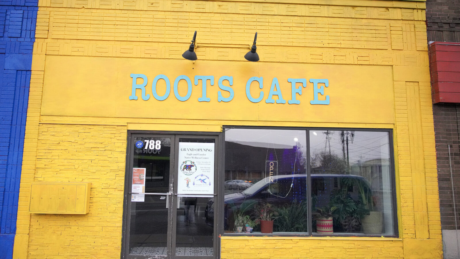 A yellow storefront with blue letters reading 'ROOTS CAFE'.